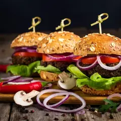 Trzy apetyczne burgery z chrupiącymi bułkami, warzywami i dodatkami na drewnianej desce.