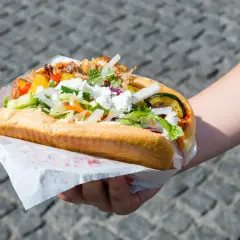 Ręka trzymająca dużego kebaba z mięsem, warzywami i serem feta.
