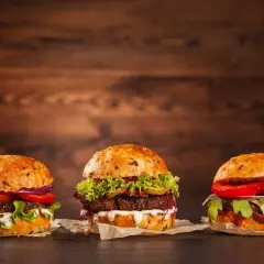 Trzy apetyczne, świeże hamburgery z warzywami i sosami na drewnianym tle.