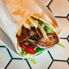 Kebab w tortilli z mięsem, frytkami, sałatą, pomidorem i cebulą na białym talerzu.