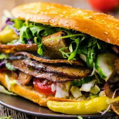 Duży kebab w bułce z mięsem, warzywami i sosem na drewnianym tle.