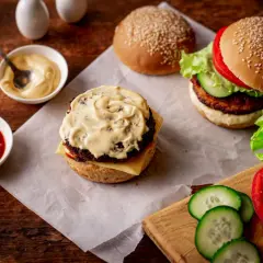Dwa burgery, sosy (majonez, ketchup) i składniki na drewnianym stole.