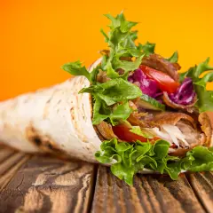 Kebab zawinięty w tortillę z warzywami na drewnianym stole.