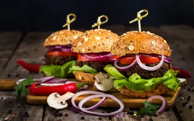 Trzy apetyczne burgery z chrupiącymi bułkami, warzywami i dodatkami na drewnianej desce.