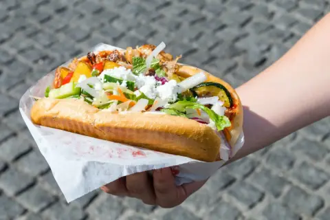 Ręka trzymająca dużego kebaba z mięsem, warzywami i serem feta.