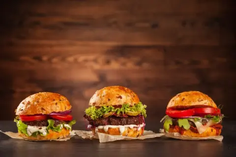 Trzy apetyczne, świeże hamburgery z warzywami i sosami na drewnianym tle.
