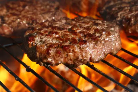 Soczyste kotlety na burgery grillujące się nad płomieniami.