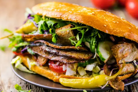Duży kebab w bułce z mięsem, warzywami i sosem na drewnianym tle.