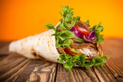 Kebab zawinięty w tortillę z warzywami na drewnianym stole.