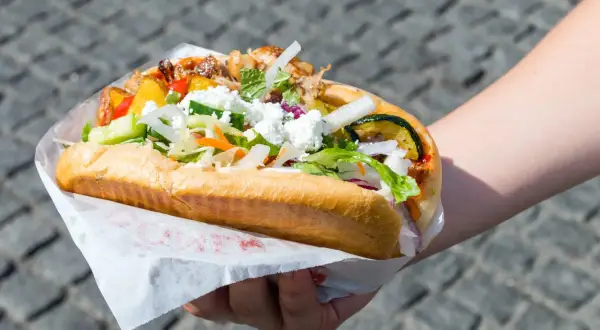 Ręka trzymająca dużego kebaba z mięsem, warzywami i serem feta.