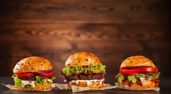 Trzy apetyczne, świeże hamburgery z warzywami i sosami na drewnianym tle.