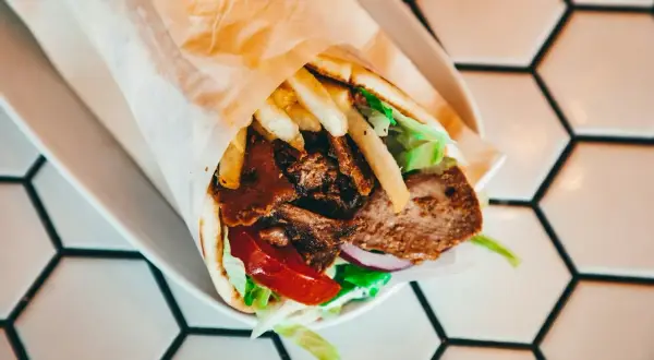 Kebab w tortilli z mięsem, frytkami, sałatą, pomidorem i cebulą na białym talerzu.
