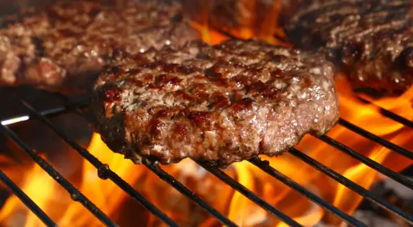 Soczyste kotlety na burgery grillujące się nad płomieniami.