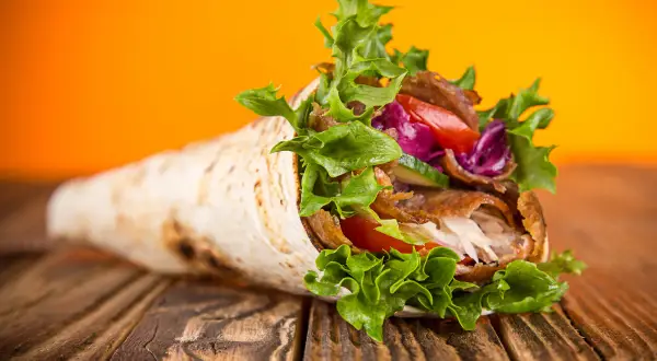 Kebab zawinięty w tortillę z warzywami na drewnianym stole.