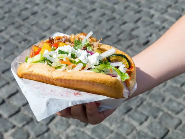 Ręka trzymająca dużego kebaba z mięsem, warzywami i serem feta.
