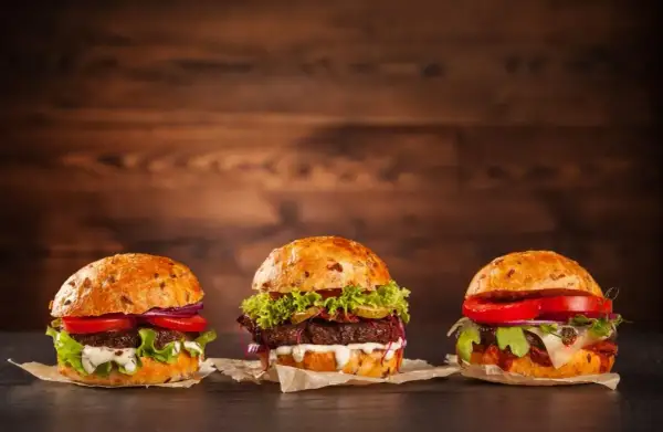 Trzy apetyczne, świeże hamburgery z warzywami i sosami na drewnianym tle.