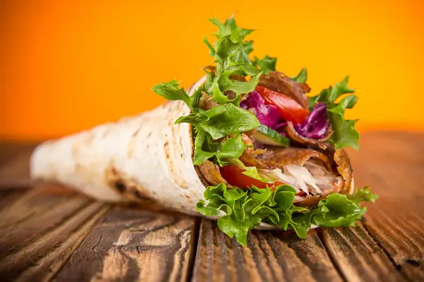 Kebab zawinięty w tortillę z warzywami na drewnianym stole.